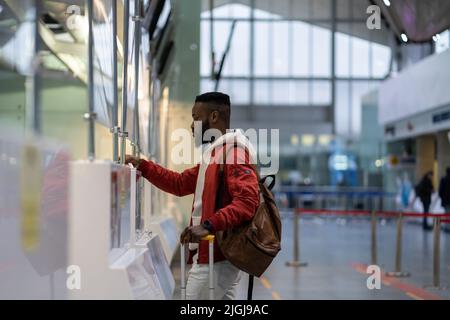 Afrikanischer junger Mann, der die Dokumente am Check-in-Schalter am Flughafen vorzeigt. Grenzkontrolle Stockfoto