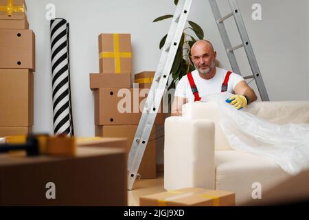 Mann Mover in uniform Verpackung Sofa für Umzug Stockfoto