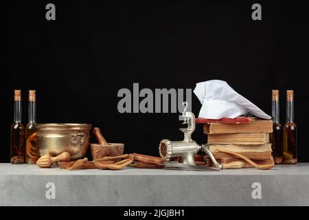 Kochmütze, alte Kochbücher und alte Küchenutensilien auf dem Küchentisch. Speicherplatz kopieren. Schwarzer Hintergrund. Stockfoto