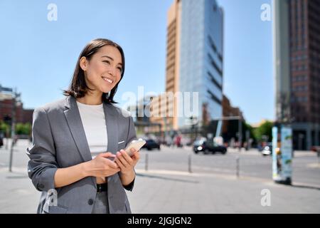 Junge lächelnde asiatische Geschäftsfrau, die auf einer großen Stadtstraße telefoniert. Stockfoto