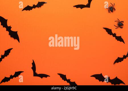 Orangefarbener Halloween-Hintergrund. Schwarm schwarzer Fledermäuse für Halloween. Schwarze Papier Fledermaus Silhouetten auf orangefarbenem Hintergrund. Halloween-Konzept, Copy Space, oben V Stockfoto