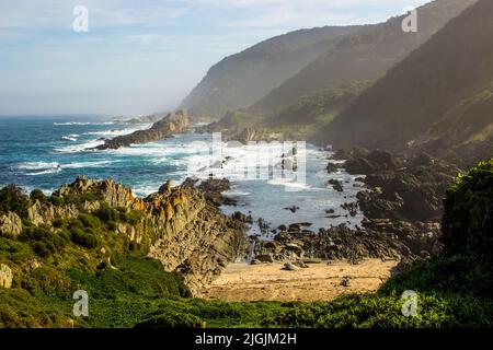 Eine kleine geschützte Bucht, versteckt zwischen den hohen Klippen und Felsen der Küste von Tsitsikamma, entlang der südlichen südafrikanischen Küste. Stockfoto