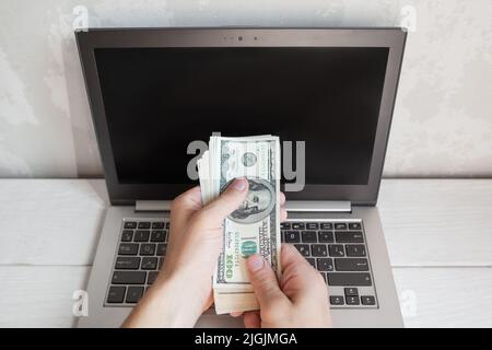 Männliche Hand steckte Dollar-Bankmoten in den Laptop-Bildschirm Stockfoto