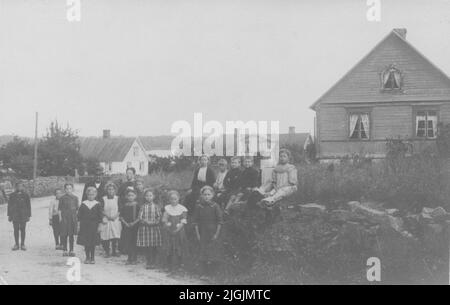 Skolklass Schulklasse mit Lehrer und Kindern aus Pukavik auf 'Riks 15'. Die Straße führt hinunter zu den Laderampen, genannt Larssons Brücken und vorbei an den Farmen von Sven Ysberg, Nils Larsson und Janne Jansson, die hier auf dem Bild zu sehen sind. Stockfoto