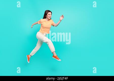 In voller Länge Foto von wunderschönen zufriedenen Mädchen laufen Sprung suchen leeren Raum auf türkisfarbenem Hintergrund isoliert Stockfoto