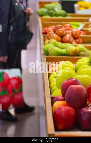 Obststand auf einem lokalen Markt mit einer Frau, die im Hintergrund eine Einkaufstasche außer Fokus hat Stockfoto