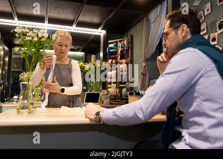 Ein Stammkunde wartet mit einer Tinktur darauf, dass der Store-Mitarbeiter seine Bestellung vorbereitet Stockfoto