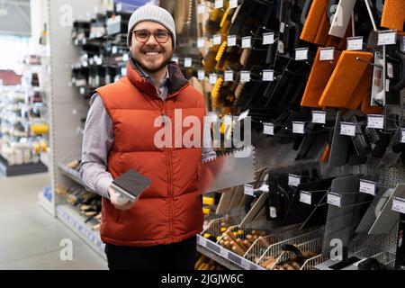 Ein Mann wählt Werkzeuge zum Putten und Verputzen von Wänden in einem Baumarkt Stockfoto