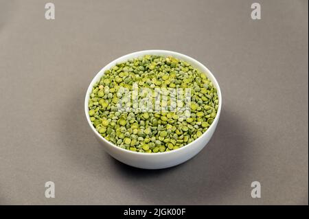 Ungekochte Speisen. Zerteilte Erbsen in einer weißen Keramikschale trocknen. Grüne Bohnen. Grauer Hintergrund. Blick von oben in einem Winkel. Selektiver Fokus. Stockfoto