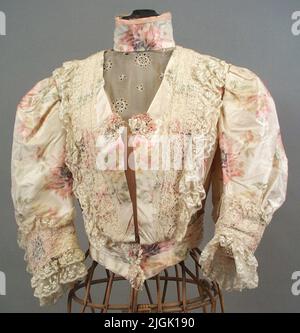 Klänningsliv Kleid Leben aus gelb-weißer Seide mit rosa Blumenmuster. Hoher Krake, kurzer Pubres mit Spitze. Falten aus transparentem Stoff mit weißer Stickerei im Hals und Ausschnitt. Rückenlänge 430 mm. „Kaiser's Fashion Store, Gothenburg“. Figuren in der Seide. Das Futter im Kragen (Seide) bröckelt. Der Anfang des 19.. Jahrhunderts. Geboren 1861-08-23, verlobt 1880. Verheiratet 1881-09-11 in Hamburg mit Großhändler Anton Ruben. Eigenes Haus auf Drottninggatan 48, Karlskrona, und das Grundstück Avvelsgärde in der Gemeinde der Loose. Frau Ruben starb am 1933-02-23. Die Objekte verwendet irgendwann du Stockfoto