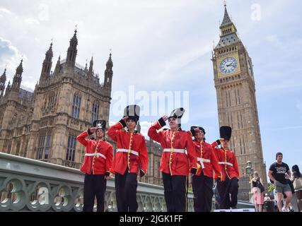 London, England, Großbritannien. 11.. Juli 2022. PETA-Aktivisten in Kostümen der Queen's Guards, mit gefälschtem Blut bedeckt und auf blutbefleckten Union Jacks stehend, protestierten vor dem Parlament auf der Westminster Bridge gegen die Verwendung von Bärenfellen in den Kappen der Queen's Guards. Derzeit verwendet das Verteidigungsministerium echtes Bärenpelz, um die Kappen zu machen, und es braucht einen Bären, um nur eine Kappe zu machen. PETA half bei der Entwicklung einer geeigneten Kunstpelzalternative, die die MOD bisher nicht verwendet hat. (Bild: © Vuk Valcic/ZUMA Press Wire) Stockfoto