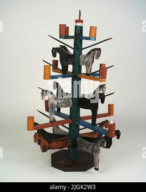 Jultäd Weihnachtsbaum aus Holz. Stiel dunkelgrün bemalt, Arme drei Runden, jeweils vier mit einem stürmischen nach oben abfallenden Arm, die Arme blau, grün und gelb, an den Enden Kerzenhalter. Auf dem Stamm 'Apfelstöcke'. Der Stamm ist in 8 Phasen geplant. Pferde auf drei Ebenen, Kontur -gesägt, in verschiedenen Farben gemalt. Im Erdgeschoss 8 Pferde, 2. Flugzeug 4 Pferde, 3. Flugzeug 4 Pferde. An der Spitze des Stammes 2 gerade oben Spitzen für Apfel?, Beine zu Hahn?. Bodenplatte 8-Rand, braun lackiert. Knochen auf Pferden im Erdgeschoss ausgeschaltet. Stockfoto