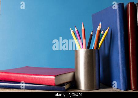 Bild von Büchern und Buntstiften im Behälter auf blauer Oberfläche Stockfoto