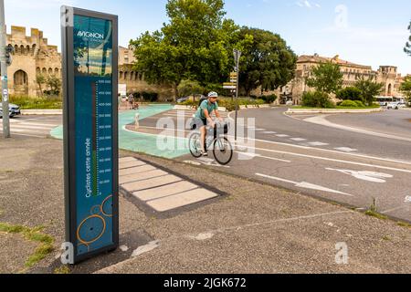 Ein Radfahrer mit Fahrradtaschen überquert die Straße in der Nähe der Porte de l'Oulle in Avignon, mit dem digitalen Radfahrerzähler und der Stadtmauer im Hintergrund, Frankreich. Stockfoto