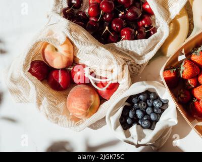 Frische Beeren in Tüten und Schachtel auf dem Tisch bei Sonnenlicht. Einkäufe im Laden vor Ort auf dem Küchentisch Stockfoto