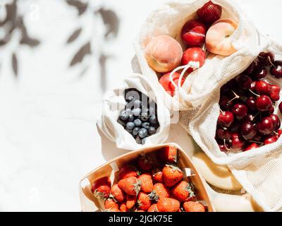 Frische Beeren in Tüten und Schachtel auf dem Tisch bei Sonnenlicht. Einkäufe im Laden vor Ort auf dem Küchentisch Stockfoto