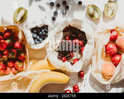 Frische Beeren in Tüten und Schachtel auf dem Tisch bei Sonnenlicht. Einkäufe im Laden vor Ort auf dem Küchentisch Stockfoto