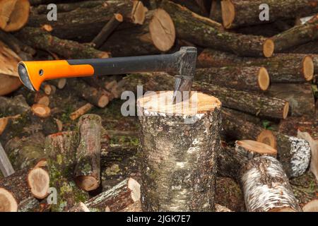 Eine spezielle Axt zum Spalten von Holz wird in den Baumstamm geklebt. Die Axt teilt das Log für die Trocknung und die anschließende Vorbereitung für den Heizschrott im Winter. Stockfoto