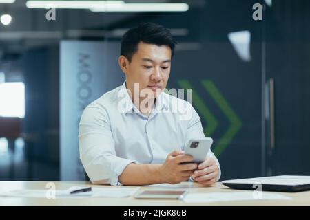 Seriöser und nachdenklicher asiatischer Geschäftsmann mit Telefon, der in einem modernen Büro telefoniert Stockfoto