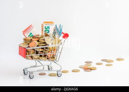 Einkaufswagen überfüllt mit Bargeld (Euro-Münzen und Banknoten). Konzepte von steigenden Preisen, Kaufkraft und steigender Inflation in Europa Stockfoto