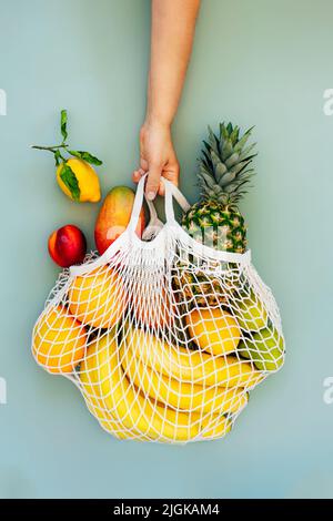 Draufsicht weibliche Hand halten Saite Tasche, Mesh-Tasche, Lebensmittelbeutel mit Bio-frischen exotischen Früchten auf hellgrünem Hintergrund. Keine Verschwendung, umweltfreundliches sh Stockfoto