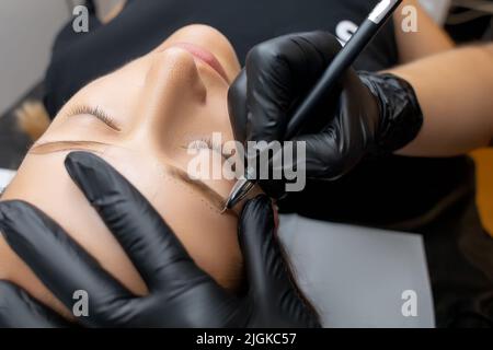 Der Meister macht mit einem Bleistift eine Kontur vor dem Augenbrauen Tattoo Verfahren Permanent Make-up Stockfoto