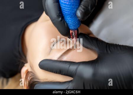 Master macht Augenbrauen Tattoo mit einem permanenten Make-up-Maschine Stockfoto