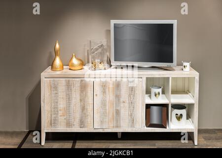 Verschiedene stilvolle Dekorationen und Fernseher mit leerem Bildschirm auf Schrank gegen beigefarbene Wand im Wohnzimmer platziert Stockfoto