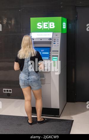 Estnische Bank; eine junge Frau, die Bargeld von einem Geldautomaten oder Geldautomaten der SEB Pank, einer estnischen Bank, Tartu, Estland, Europa, erhält Stockfoto