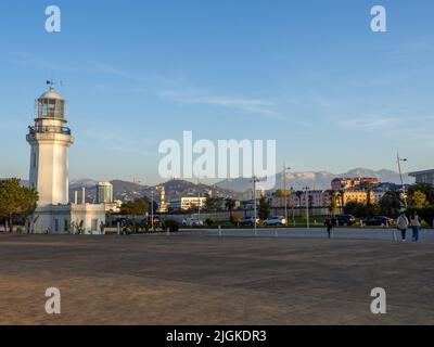 Weißer Leuchtturm in der Stadt vor der Kulisse der Berge. Stadtumgebung. Wunderschöne Straßenlandschaft Stockfoto