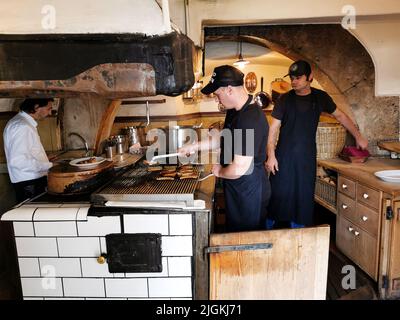 Regensburg, DEUTSCHLAND - 09.17.2019: Männliche Köche kochen mit traditionellen deutschen Würsten auf dem Grill in einer Kneipenküche. Stockfoto