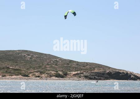 Professioneller Kite-Surfer reitet auf einem Brett mit Planke auf einem See mit Meerwasser bei Sonnenuntergang. Wasserspritzer und Sonneneinstrahlung. Wassersport. Panoramablick Stockfoto