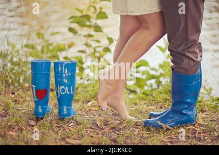 Blaue Gummistiefel mit der Aufschrift I love you stehen im Wald auf dem Gras. Liebevolles Paar, das Seite an Seite steht. Konzept oder Postkarte der Liebe Stockfoto