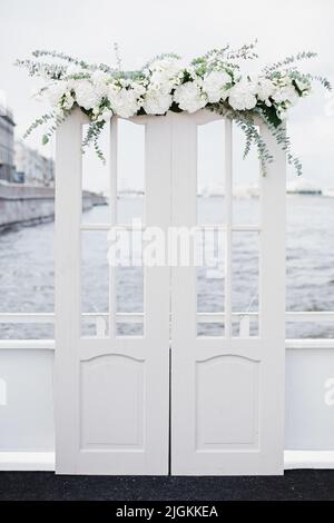 Eleganter Hochzeitsbogen mit frischen Blumen vor dem Hintergrund des Ozeans und des blauen Himmels. Bogen mit Blumen geschmückt steht in der luxuriösen Bereich der Stockfoto