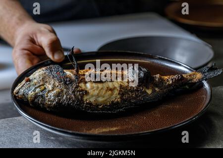 Prozess des Grillens von Fisch aus der ganzen Meeresbrasse auf einem Grill über heißer Kohle. Gegrillter Dorado Stockfoto