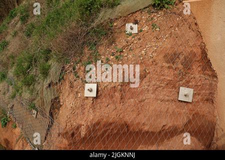 Die Nahaufnahme des Netzes und der Gesteinsarbeiten über dem Jurassic-Felsen aus rotem Sandstein bei Sidmouth in Devon ist Teil der neuen Alma Bridge-Entwicklung und wird vor der Entwicklung stehen Stockfoto