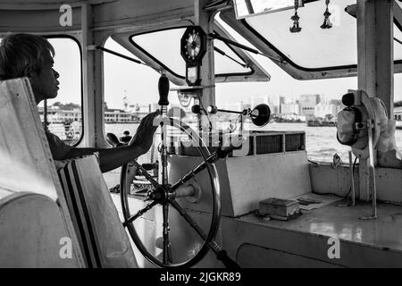 Bangkok, Thailand - 11. Dezember 2009: Fährmann steuert die öffentliche Fähre auf dem Chao Praya Fluss in Bangkok. Schwarzweiß-Fotografie Stockfoto