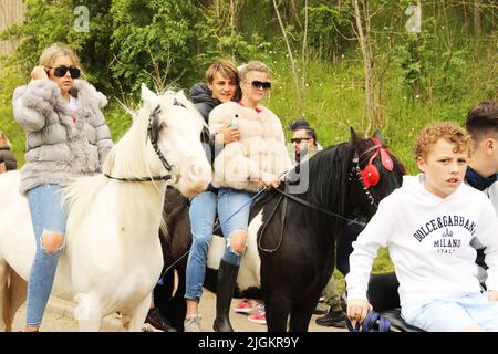 Teenager, die zu Pferd sind und Sonnenbrillen und Pelzmäntel tragen, reiten durch Appleby, Appleby Horse Fair und Appleby in Westmorland, Cumbria Stockfoto