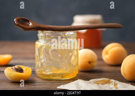 Leeres Glas mit verzehrter Aprikosenmarmelade. Leeres Glas mit hausgemachter Aprikosenmarmelade, Löffel und reifen Aprikosenfrüchten auf dem Küchentisch. Stockfoto