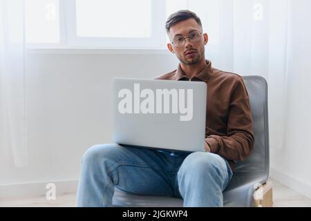 Ernst verwirrt attraktiver nachdenklicher junger Mann in einer Brille mit Laptop sieht die Kamera im Heimbüro an. Modernes Berufsangebot. Remote-Job Entfernt Stockfoto