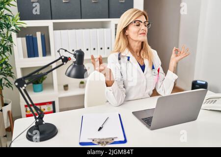Blonde Frau mittleren Alters in der Ärzteinform, die in der Klinik Yoga-Übungen macht Stockfoto