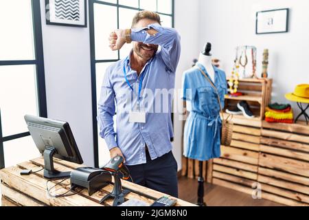 Mann mittleren Alters, der als Manager in der Einzelhandelsboutique arbeitet, lächelt fröhlich und guckst einen Buh mit Händen, die Gesicht zeigen. Überrascht und begeistert Stockfoto