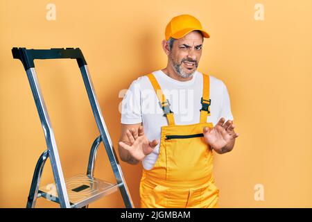 Schöner Mann mittleren Alters mit grauen Haaren hält Leiter angewiderten Ausdruck, unzufrieden und ängstlich tun Ekel Gesicht, weil Abneigung Reaktion. Mit Stockfoto