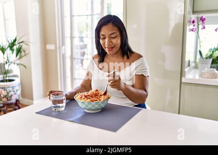 Hispanische Brünette Frau essen Spaghetti in der Küche Stockfoto