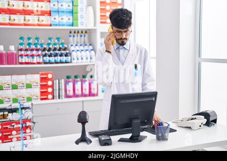 Junger hispanischer Apotheker, der auf dem Smartphone spricht und in der Apotheke arbeitet Stockfoto