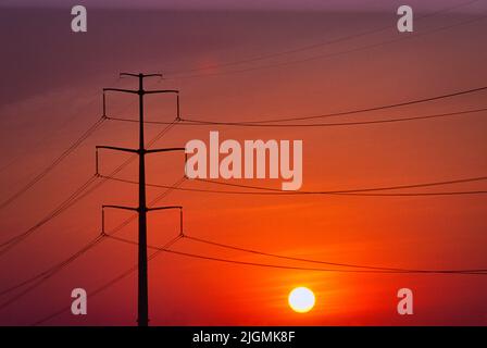 Hochspannungsleitungen transportieren Energie durch die Landschaft, wenn die Sonne untergeht. Stockfoto