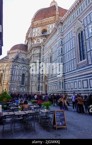 Leute in der Schlange, entlang der Seite der großen Kathedrale, warten darauf, den Dom zu betreten, während andere an Restauranttischen im Freien sitzen, Florenz, Italien. Stockfoto