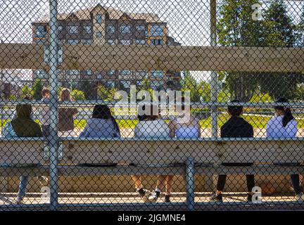 Sommeraktivitäten für Schüler. Kinder spielen Fußball, Fußball im Freiluftstadion. Eine Gruppe von Studenten, die sich ein Sportereignis im Stadion ansehen. Street phot Stockfoto