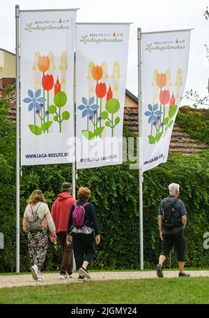 Beelitz, Deutschland. 08.. Juli 2022. Besucher laufen unter Fahnen mit dem Logo der State Garden Show Laga. (To dpa: Bisher 230.000 Besucher auf der State Garden Show in Beelitz) Quelle: Jens Kalaene/dpa/Alamy Live News Stockfoto