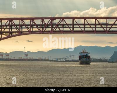 Am späten Nachmittag scheint die Sonne hinter dem Containerschiff, das in den Hafen eindringt Stockfoto